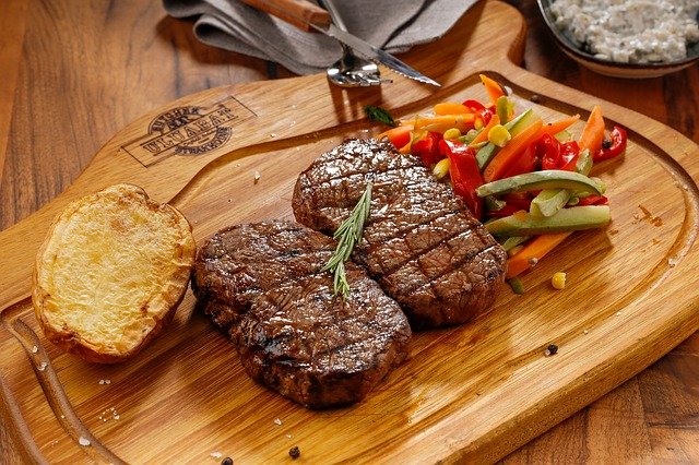 steak se zeleninou a přílohou na dřevěném podnose v restauraci